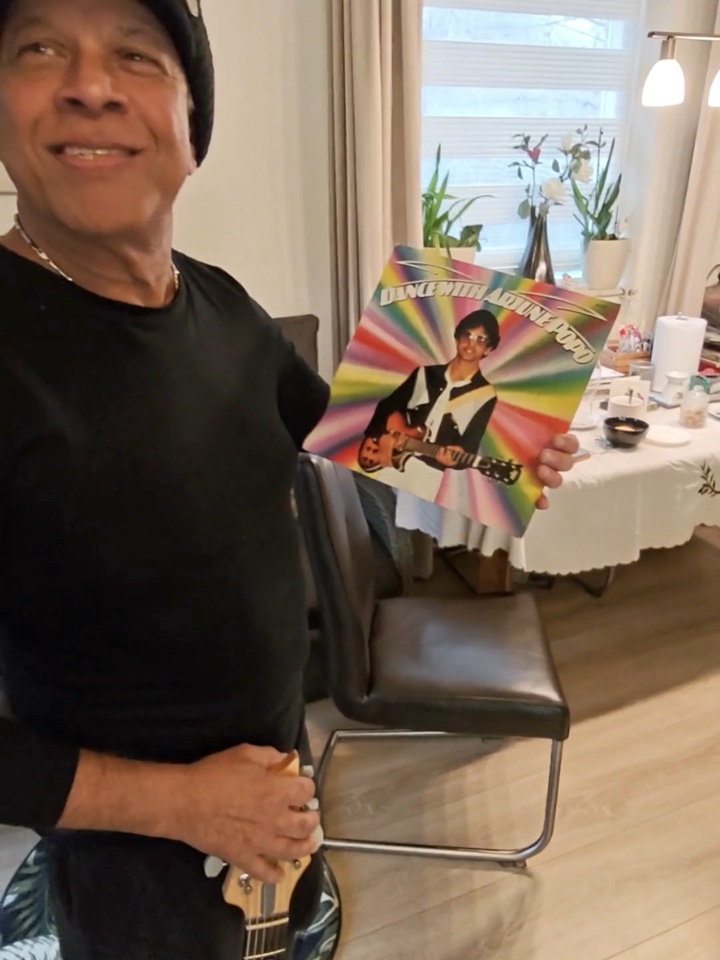 Krishn Malhoe at home, smiling, holding up the Dance With Arjune Popo LP