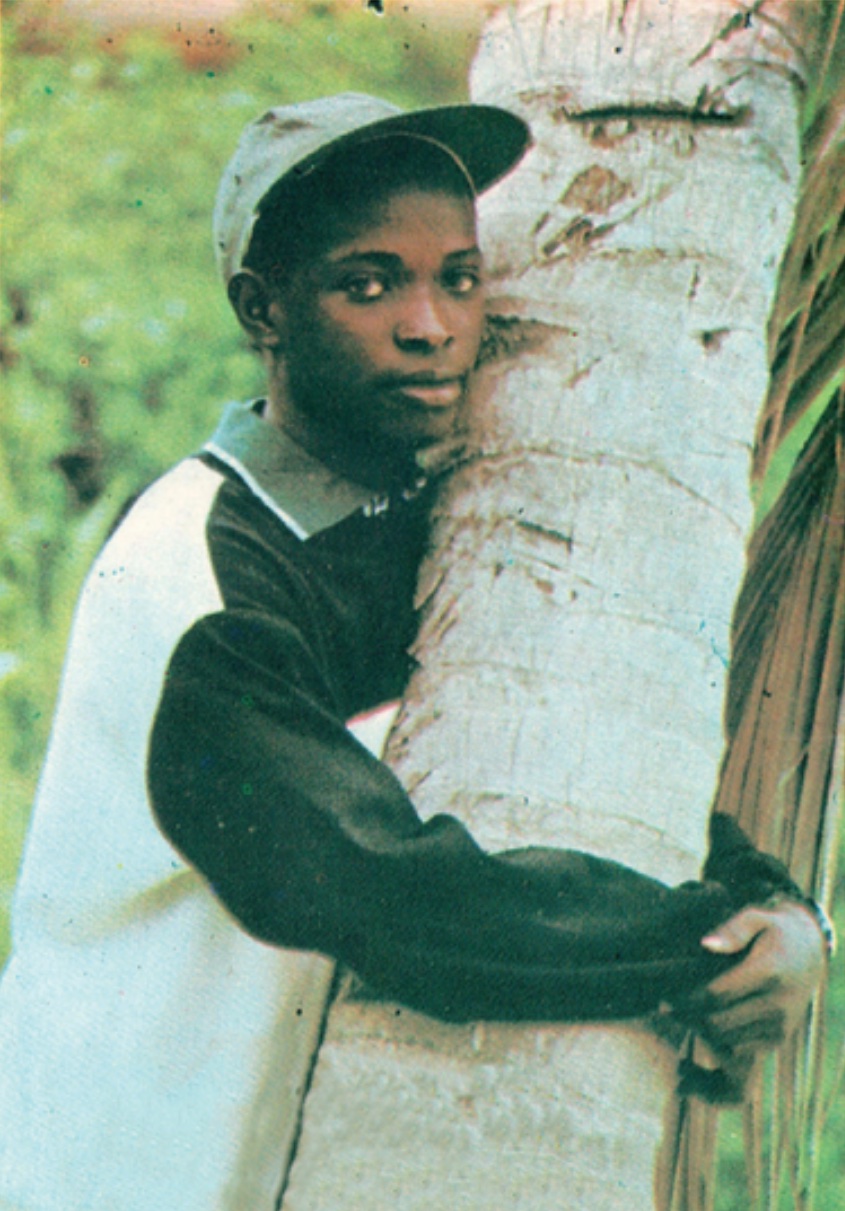 A young Hamed Farras in a cap, hugging a palm tree
